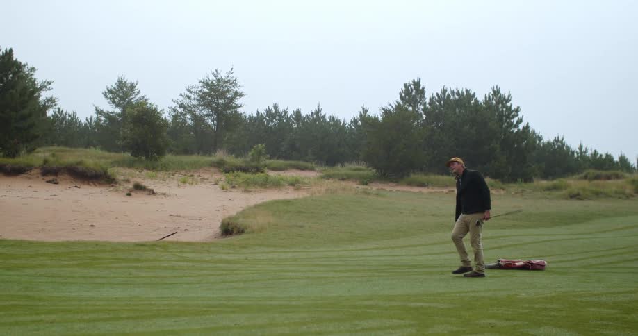 Man drives golf club across golf course and smiles in direction the ball went
