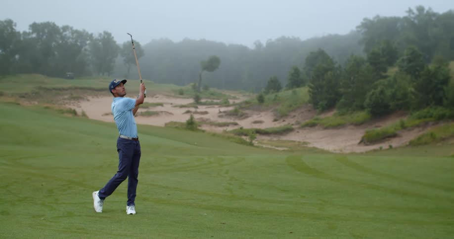Golfer hits a golf ball with an iron at daytime
