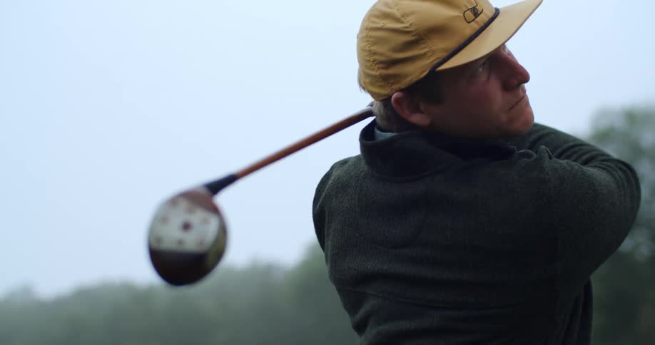 A determined man swings a golf club then watches for the ball to drop