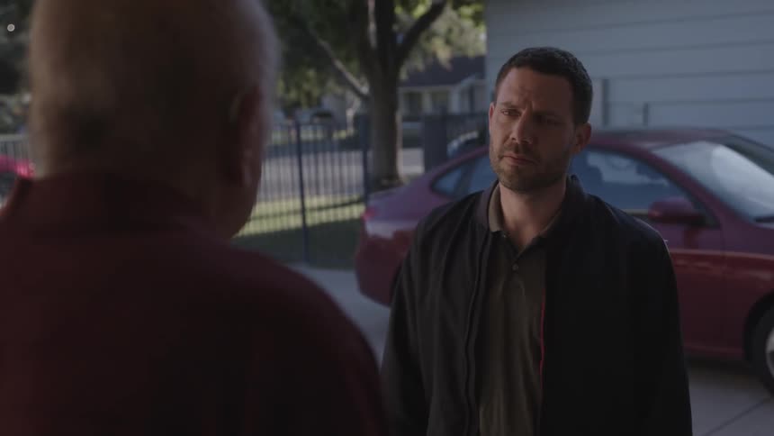 A man standing in a driveway looks sad and apologetic as he talks to an elderly man in front of him