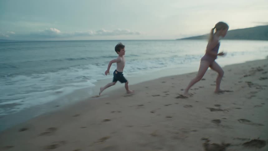 Mother watches son and daughter run across beach leaving footprints