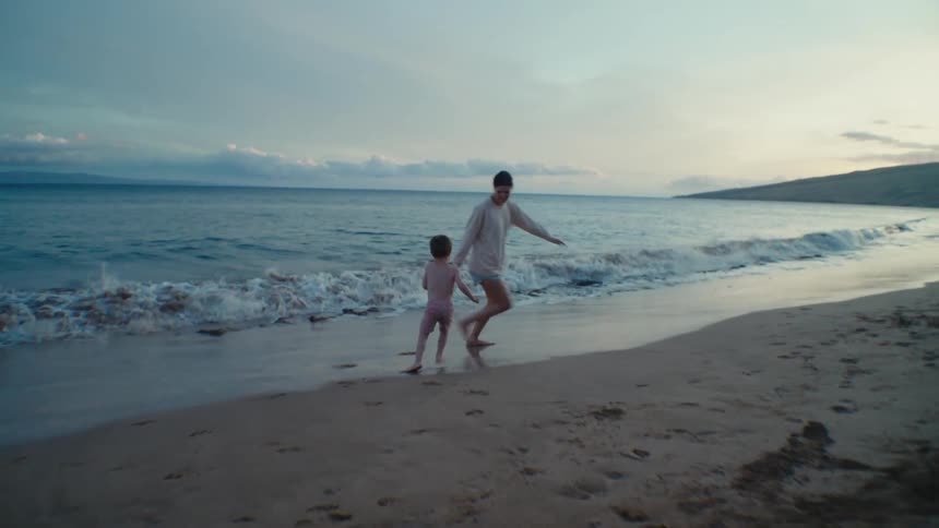 A woman playfully chases her son as they wade in the ocean