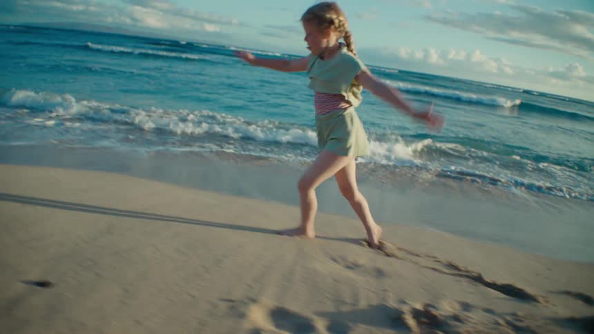 Blonde girl with braids turns a cartwheel on the beach at sunset