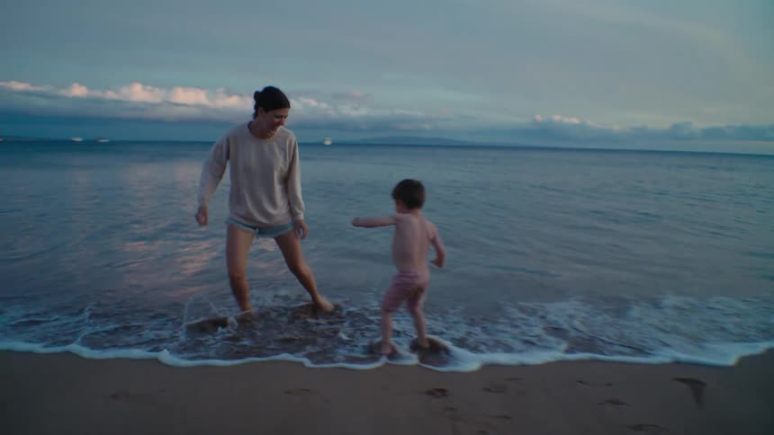 A woman and a young boy play at the waters edge on a beach laughing and chasing each other