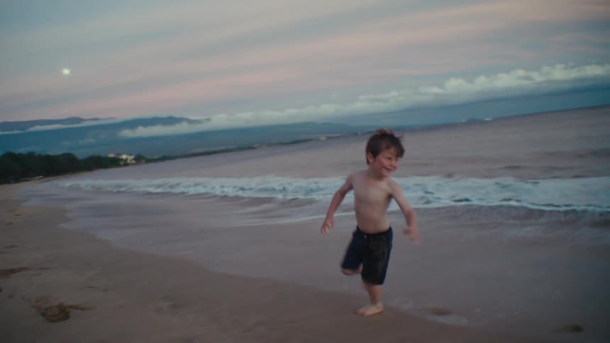 Two kids chase each other along the beach at dusk