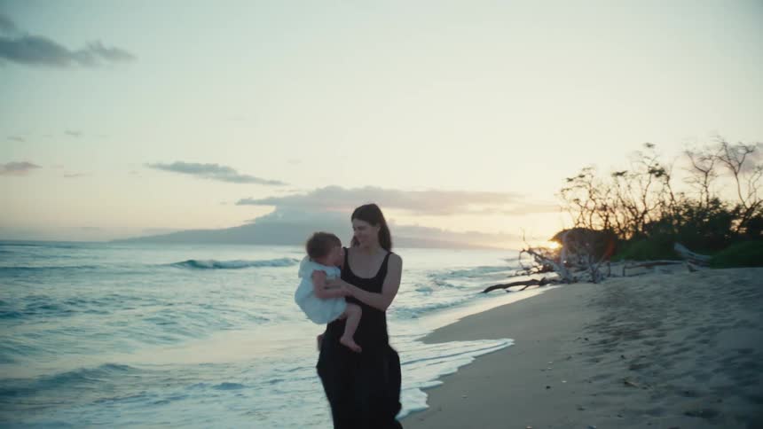 A woman spins her daughter around on the beach
