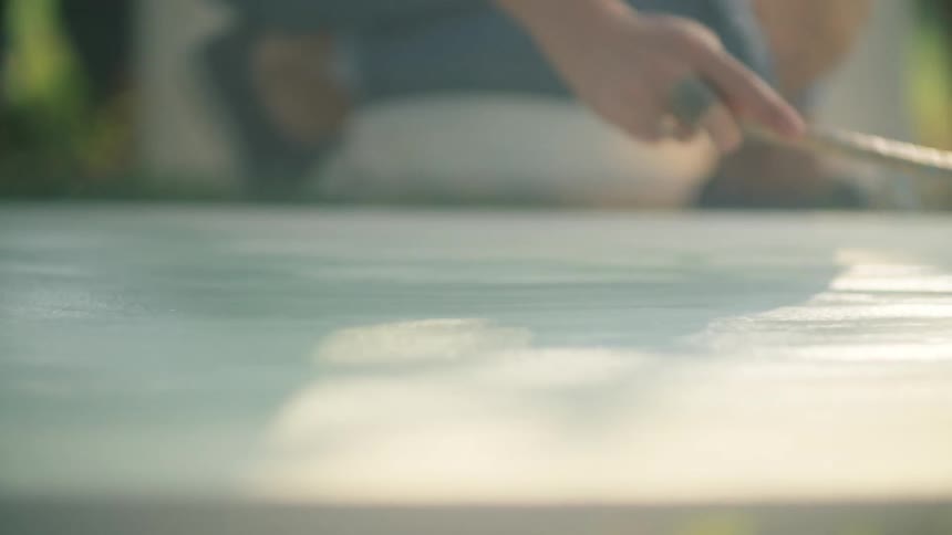 A person is painting a large canvas on the ground
