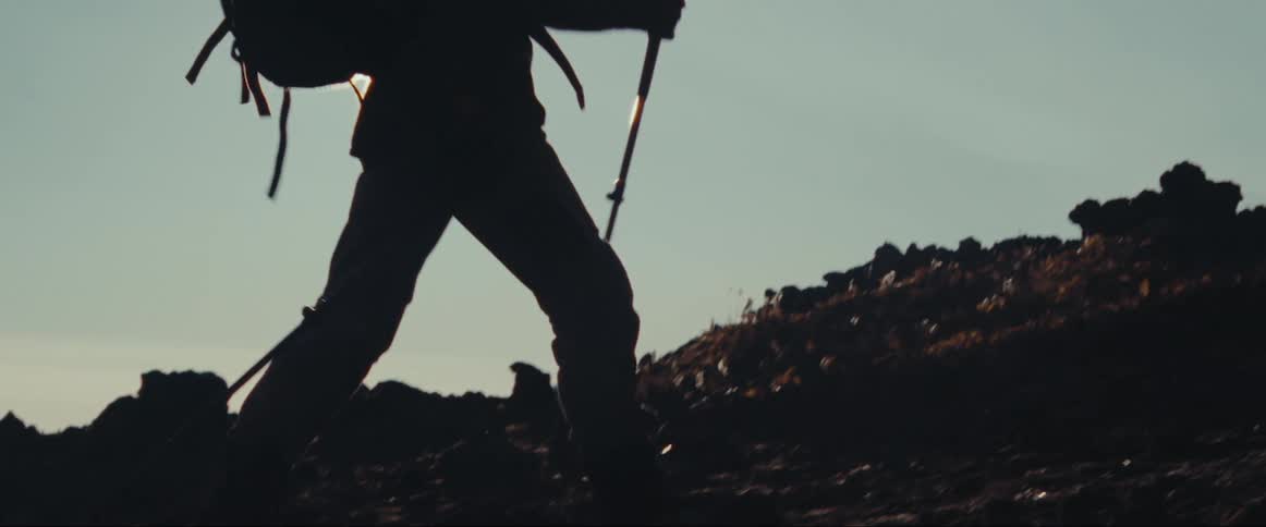 A hiker uses walking sticks to walk through a rocky path