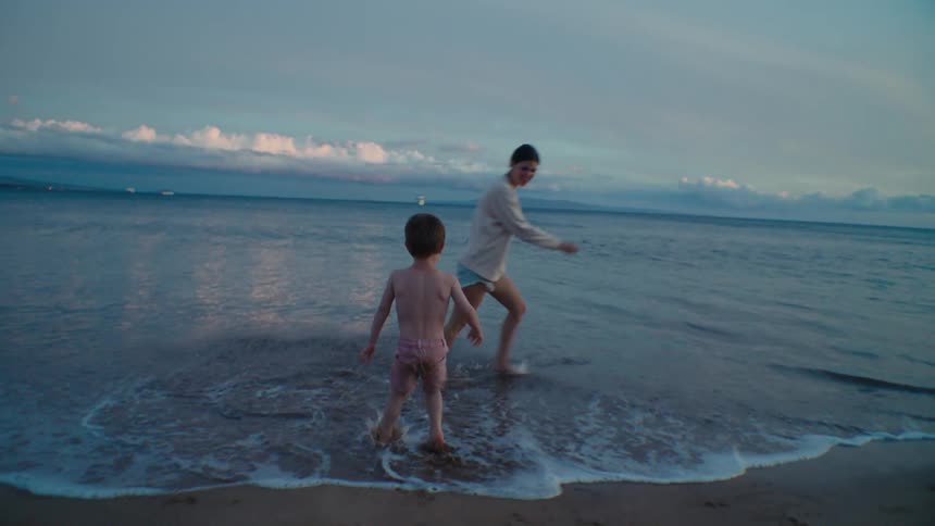 Mother and son play on the beach at dusk near the ocean