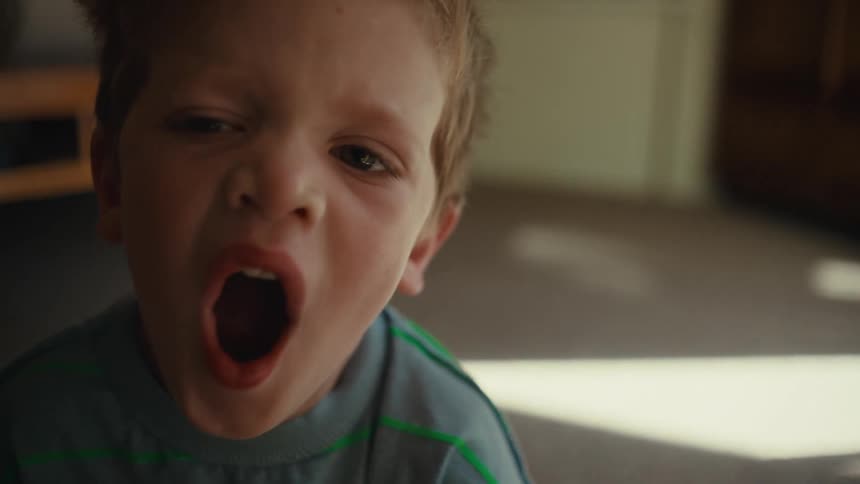 Young boy yawns while sitting on carpet in home