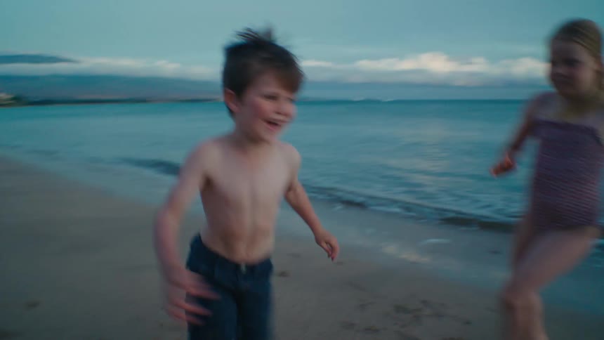 A little girl chases a little boy down the shoreline of a beach