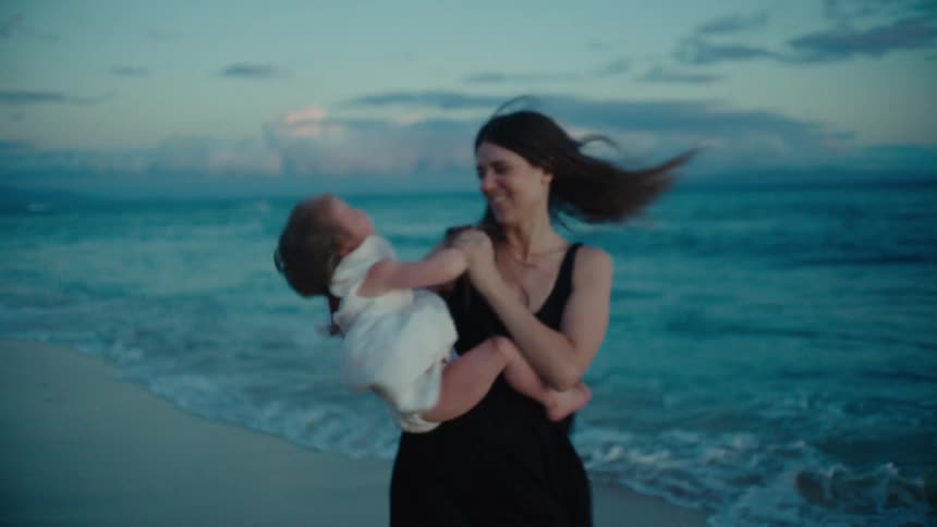 A woman spins around with her baby on the beach