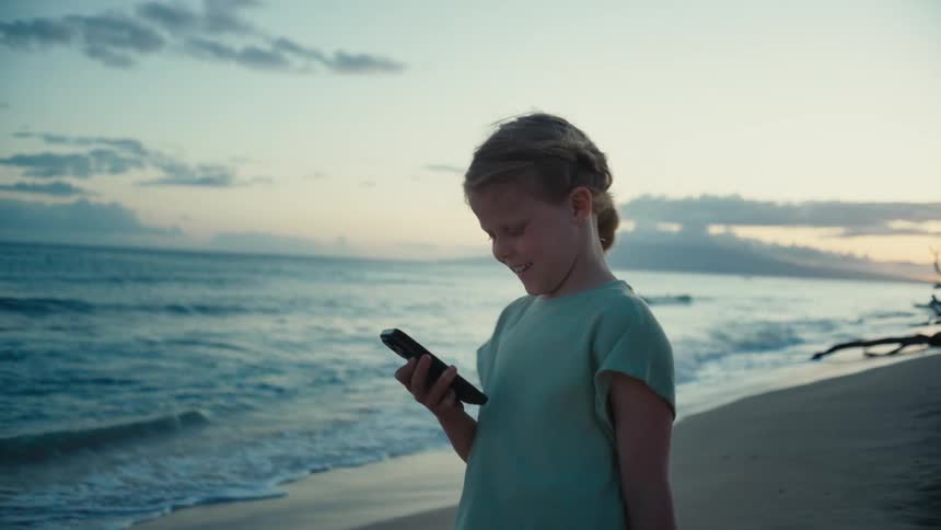 A girl is using her phone on the beach