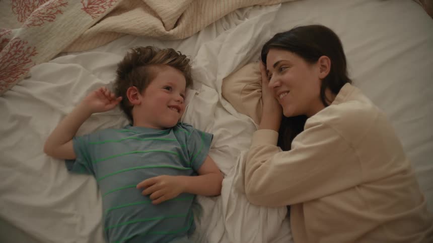 Mother and son lie on bed talking and smiling