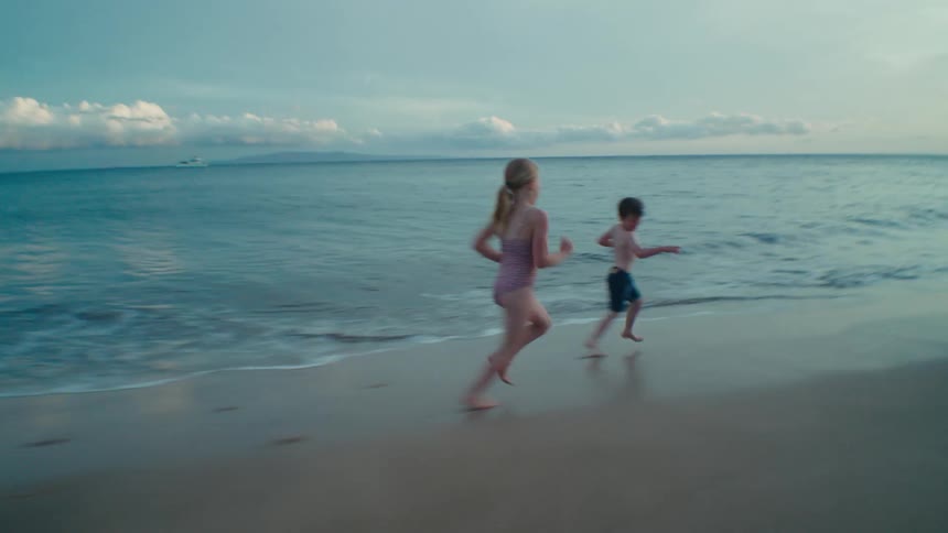 Children run on the beach along the water