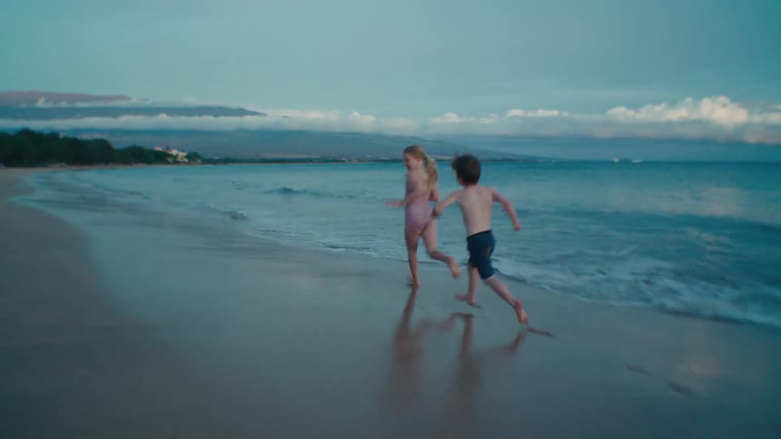 A boy playfully chases a slightly older girl along a beach during the day