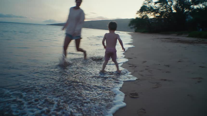 A young boy chases a woman around a beach as she playfully evades him