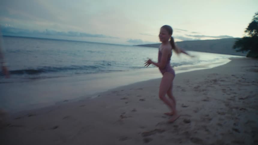 young girl does cartwheel on beach with her mom