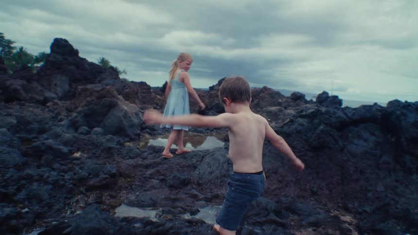 Two children climb over the rocks on the shore