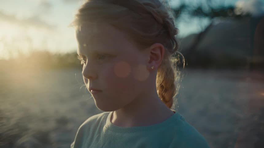 A young girl on a beach is staring at the ocean when her mother comes from behind and gently grabs her shoulders