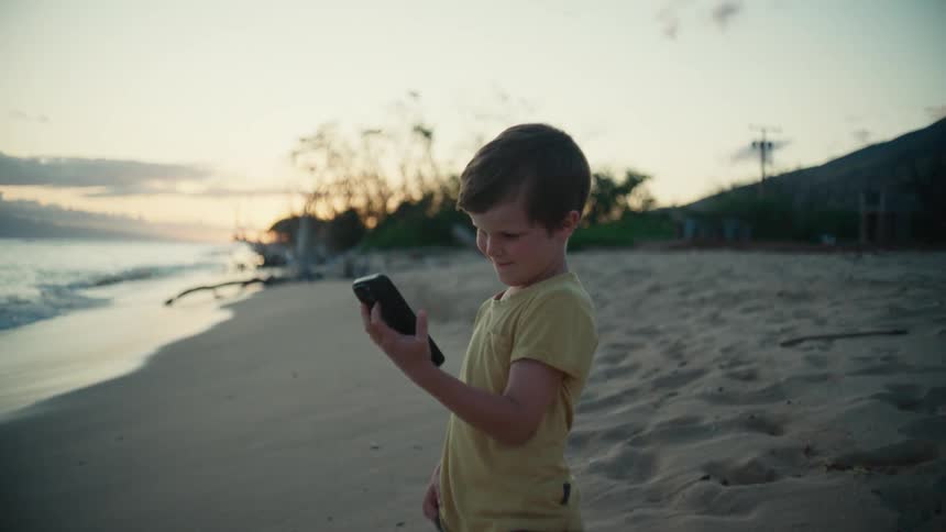 A boy looks at a smartphone on the beach