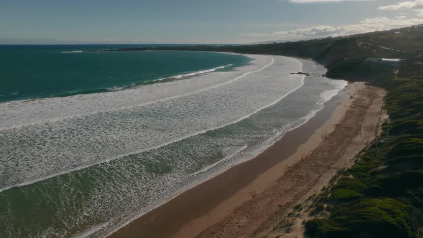 Surf flows onto beach near hills and town under a cloudy sky