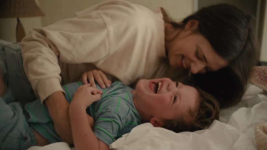 Mother tickles laughing son as they lie on the bed
