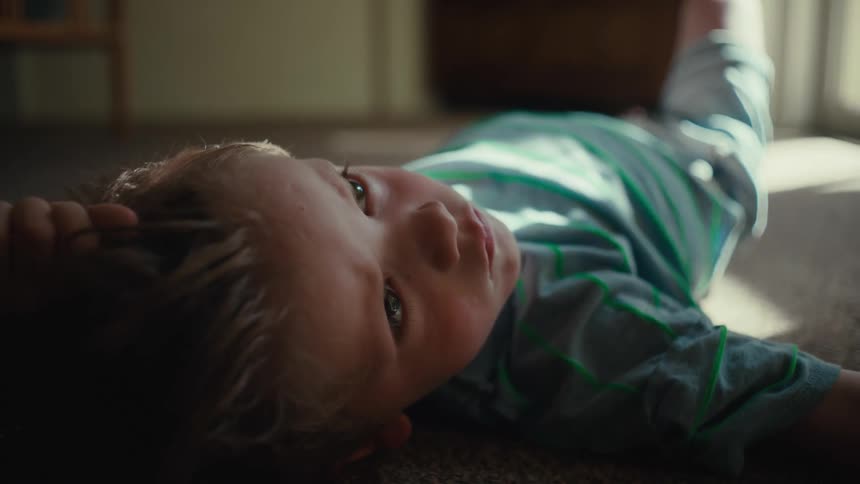 A young boy lying on the floor looks pensive then coughs