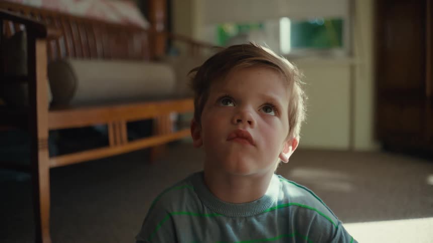 A toddler sits on the floor of his room and stares at the ceiling