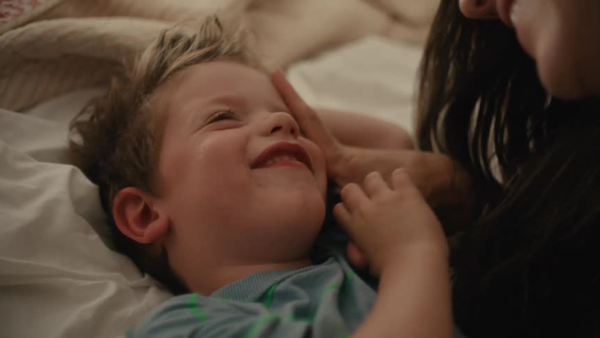 A mother and her son are laying down while laughing and the mom kisses him on the forehead