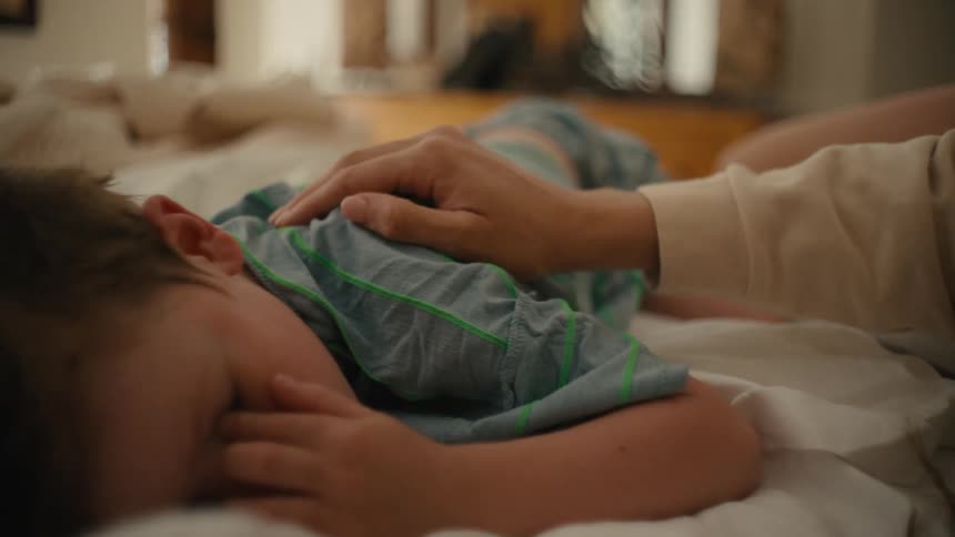 Mother strokes shoulder and head of boy waking from a nap