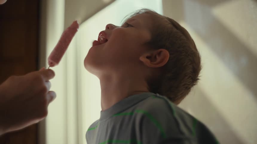 A woman shares an ice cream with her toddler son as they both take turns licking it