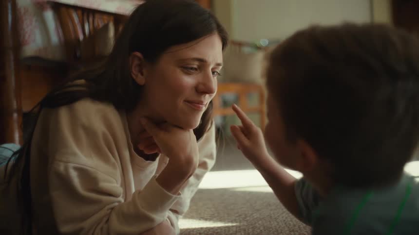 A boy touches his moms nose while lying on the ground
