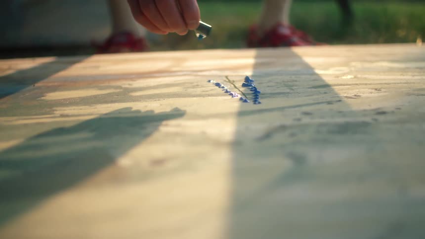 Artist leans down to apply color onto canvas lying on grass