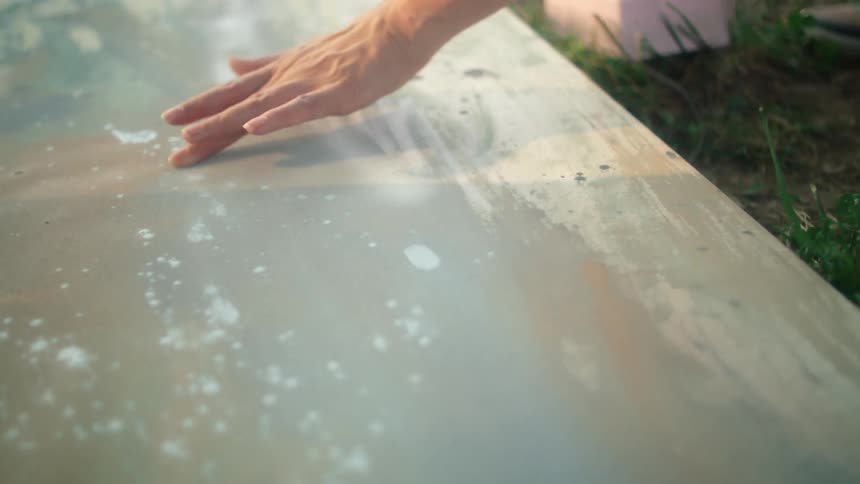A womans hand is showing her carefully smudging paint onto a large canvas while she is outside in the grass