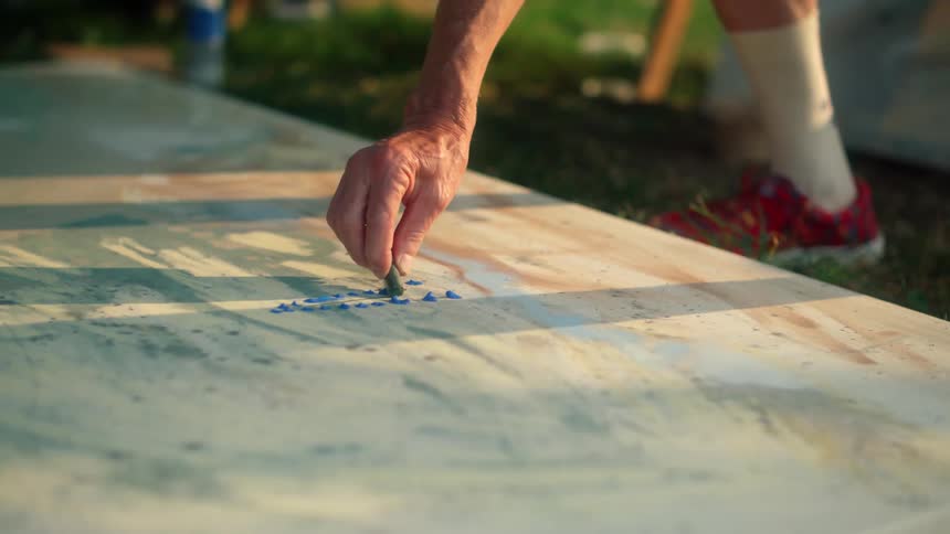Older artist runs pastel across canvas lying on lawn