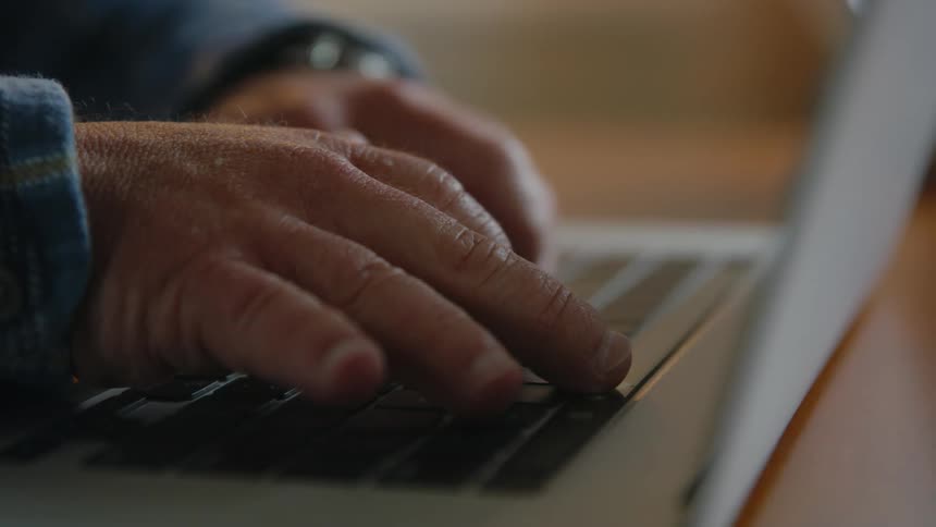 Man with thick fingers manipulates laptop keyboard while sitting at table