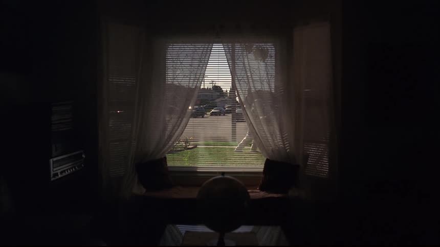 Window of dimly lit room shows person in astronaut spacesuit mowing the lawn with a reel mower