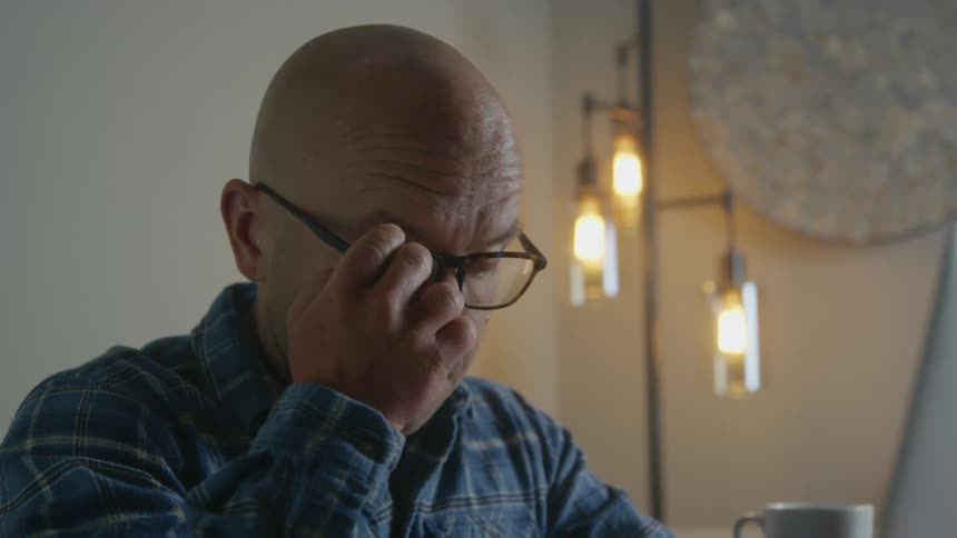 Man working on laptop rubs his eyes
