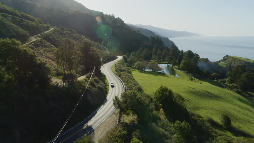 Car drives along one of multiple highways on mountain near coast on sunny day