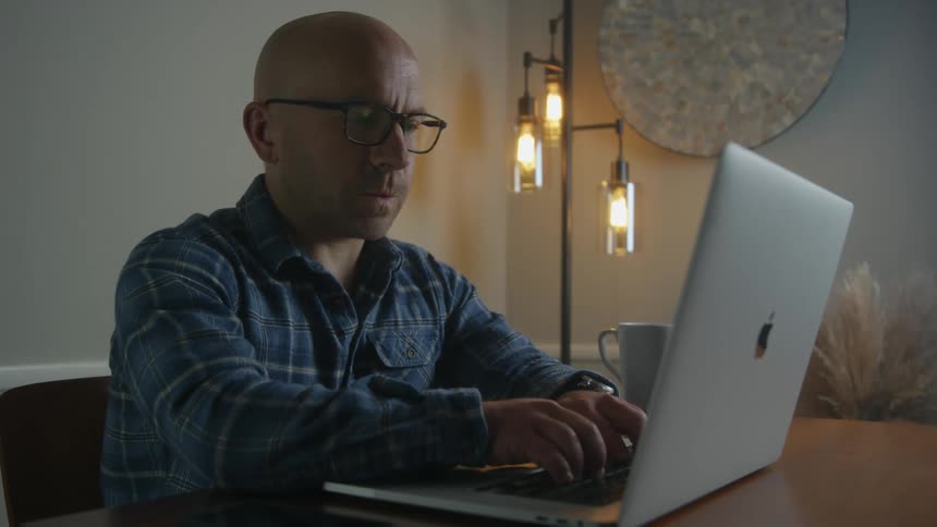 Man sits at table typing on apple laptop