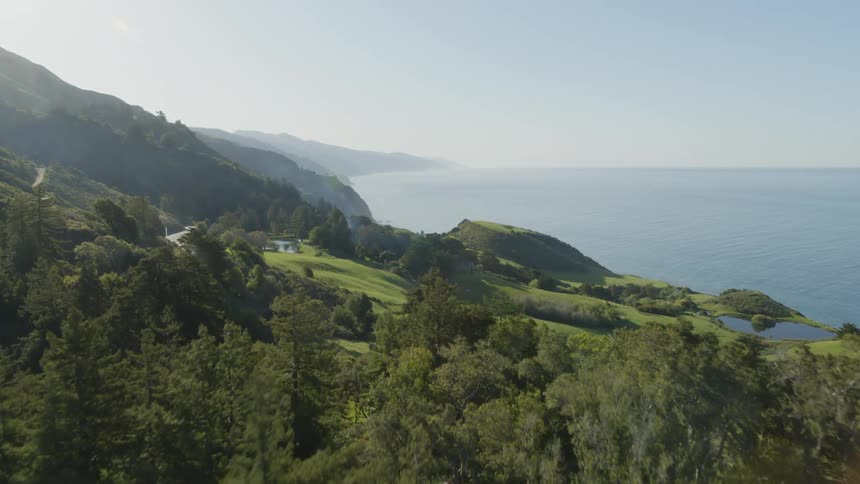 Scattered woods cover hills and mountains on coast on misty day