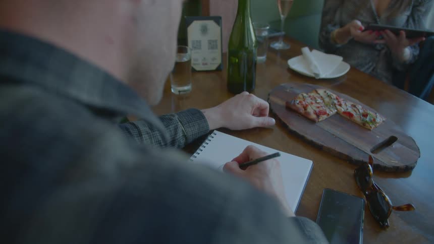 A man sketches while sitting at a restaurant