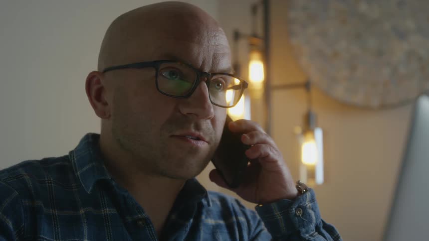 A man talks on the phone while sitting in front of his laptop