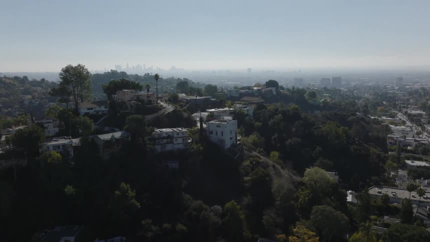 Apartment buildings on hills tower over residential neighborhood a distance from foggy city skyline
