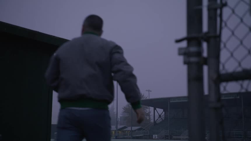 Man slides open gate and walks toward viewing stands near snow covered buildings