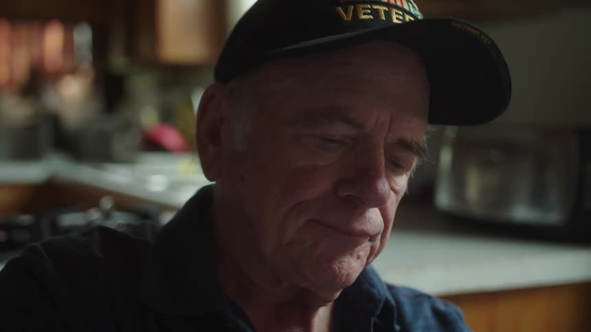 Elderly man sits near kitchen sighing and staring