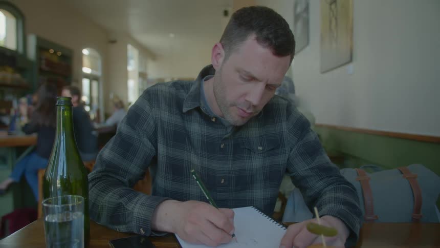 Man sits at table in restaurant sketching in sketchbook