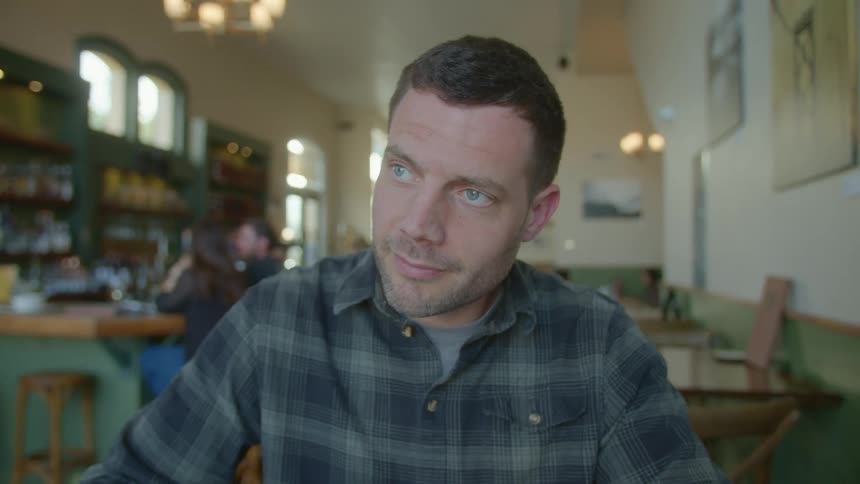 Man sitting in restaurant looks up from his sketching to smile