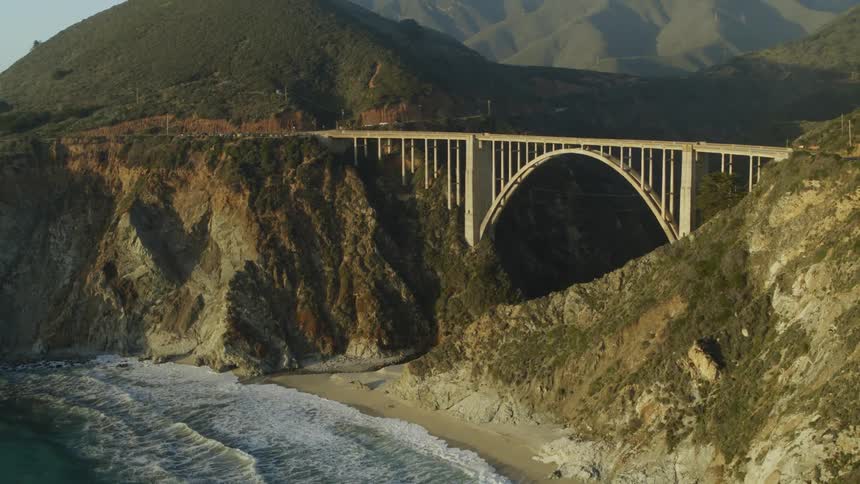 Beautiful drone of Big Sur waves roll onto beach near Bixby bridge filling gap between mountains on misty day